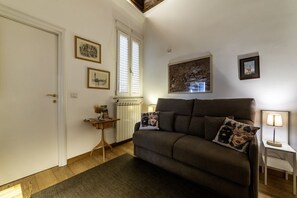 A living room with a sofa, a small side table, a radiator, and framed pictures on the wall.