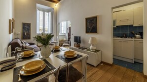 A dining area with a table set for four, a sofa, a TV, and a kitchen visible through an open door. - Minerva 5 - FromHometoRome (Roma)
