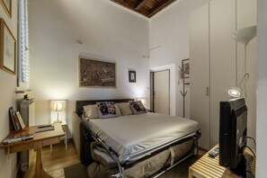 Een slaapkamer met een bed, nachtkastje, lamp en een televisie.
