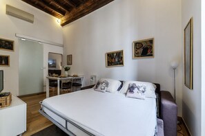 A bedroom with a bed, a desk, and chairs. There are paintings on the wall.