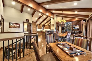 A spacious dining area with wooden tables and chairs, a stone accent wall, and a view of the kitchen in the background.