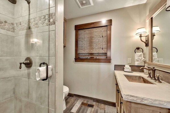 Un baño con ducha, inodoro y tocador con espejo y dos lavabos.