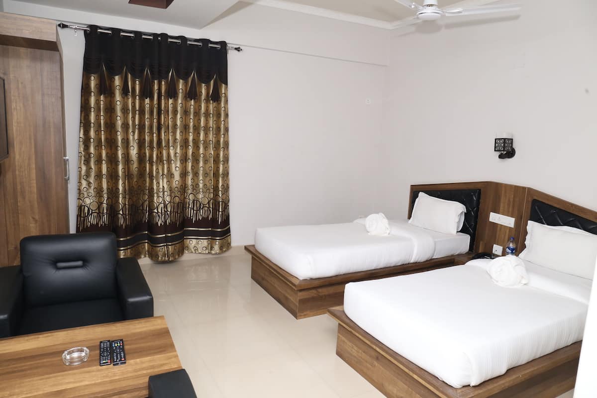 A hotel room with two single beds, a wooden desk with a chair, a TV, and a ceiling fan.