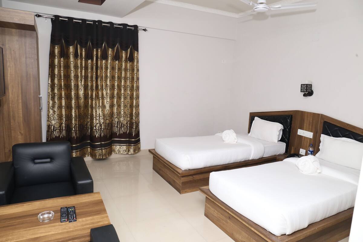 A hotel room with two beds, a desk with a chair, a TV, and a ceiling fan.