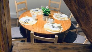 Una mesa de madera redonda dispuesta para cuatro personas, con individuales blancos, platos y cubiertos. Una planta en maceta se encuentra centrada sobre la mesa.