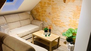 Un acogedor espacio tipo loft con pared de piedra, viga de madera en el techo, sofá, mesa de centro y planta en maceta.