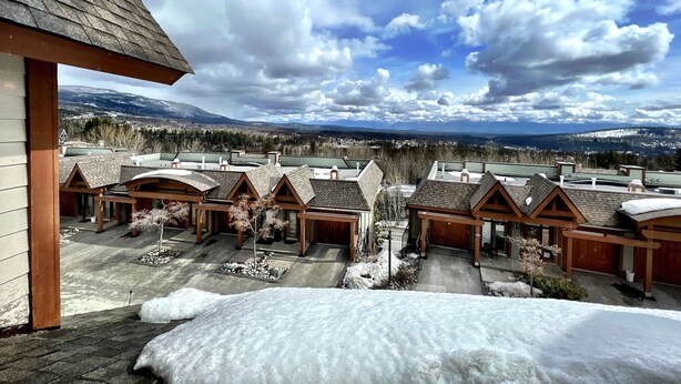 A view of a resort with multiple chalet-style buildings, a snowy landscape, and a mountainous backdrop.