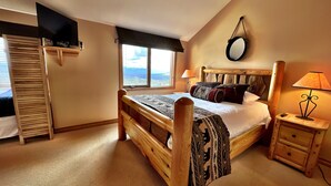 A bedroom with a wooden bed, a nightstand, a lamp, a window with a view, and a wardrobe.