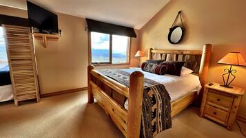 Une chambre à coucher avec un lit en bois, une table de chevet, une lampe, une fenêtre donnant sur un beau paysage et une armoire.