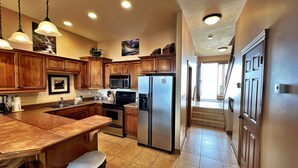 A kitchen with wooden cabinets, stainless steel appliances, a tiled floor, and pendant lighting.