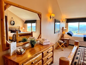 A cabin with a wooden bed, a wooden dresser, a mirror, and a view of the mountains.