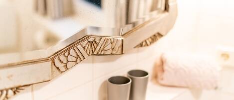 A bathroom with a mirror, two grey cups on a shelf, and a pink towel on the floor.
