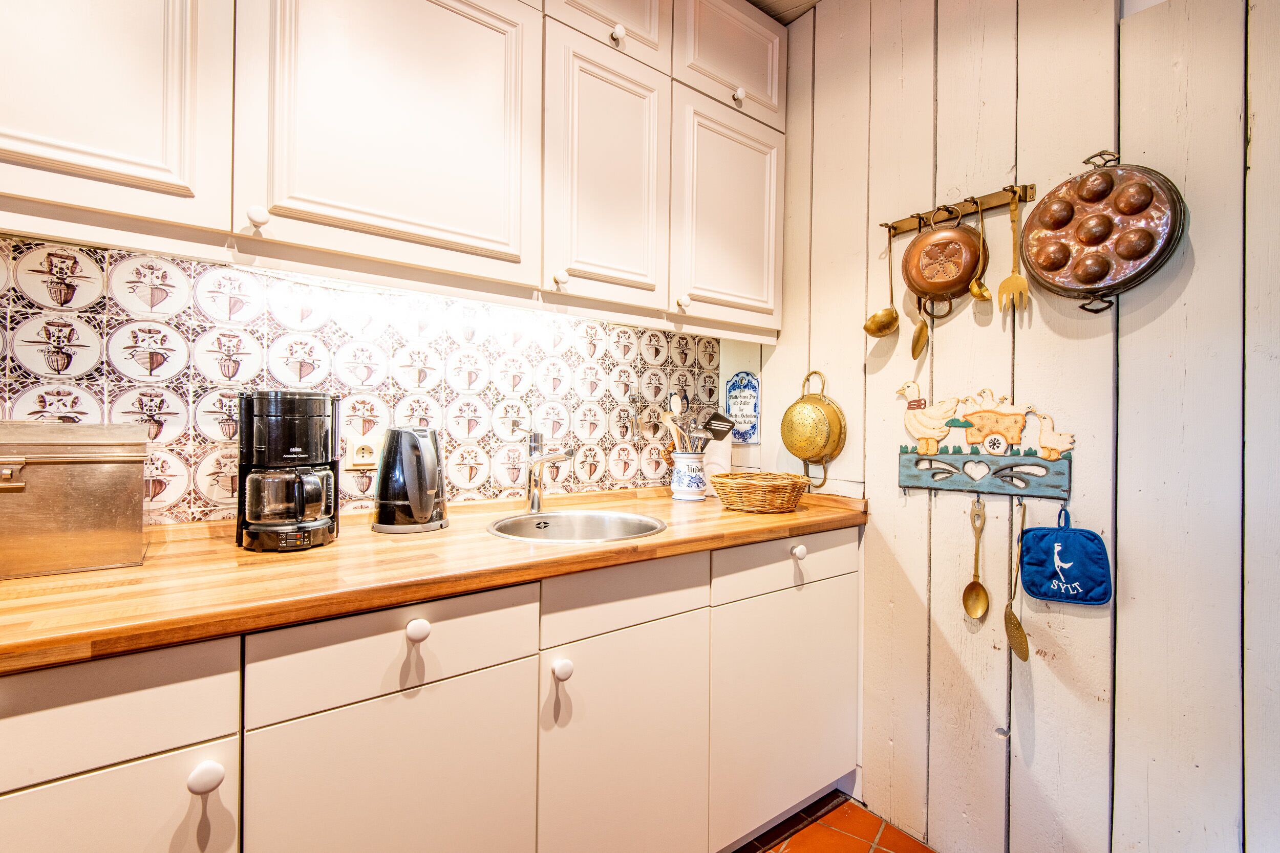 A kitchen with white cabinets, a wooden countertop, a coffee maker, a sink, and decorative items on the wall.