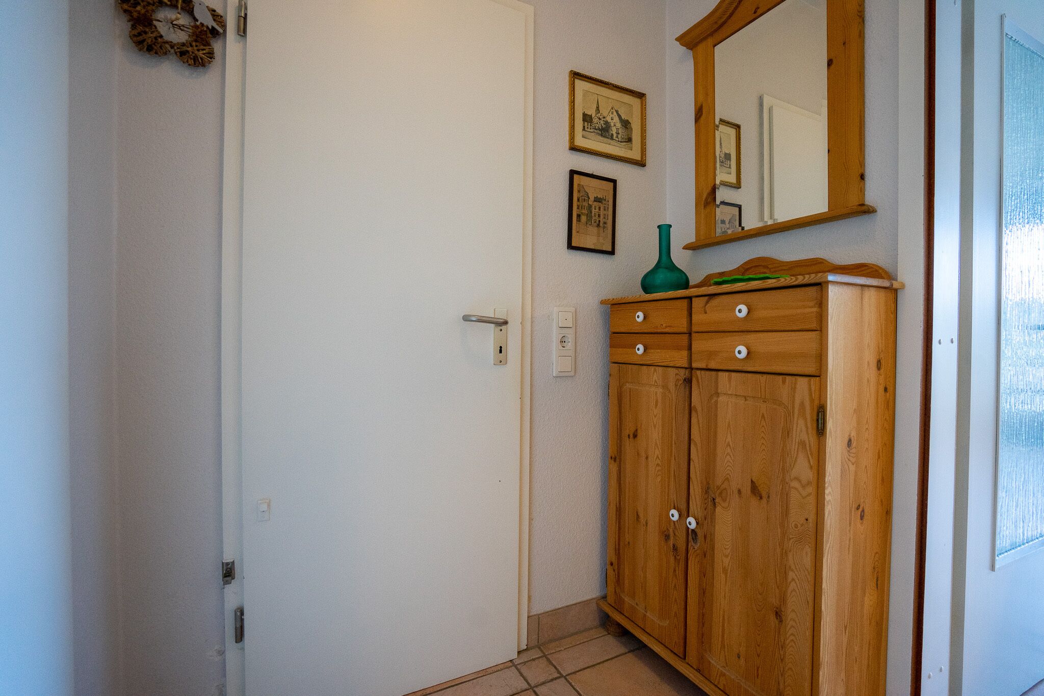 A room with a wooden wardrobe, a door, and a wall-mounted mirror.