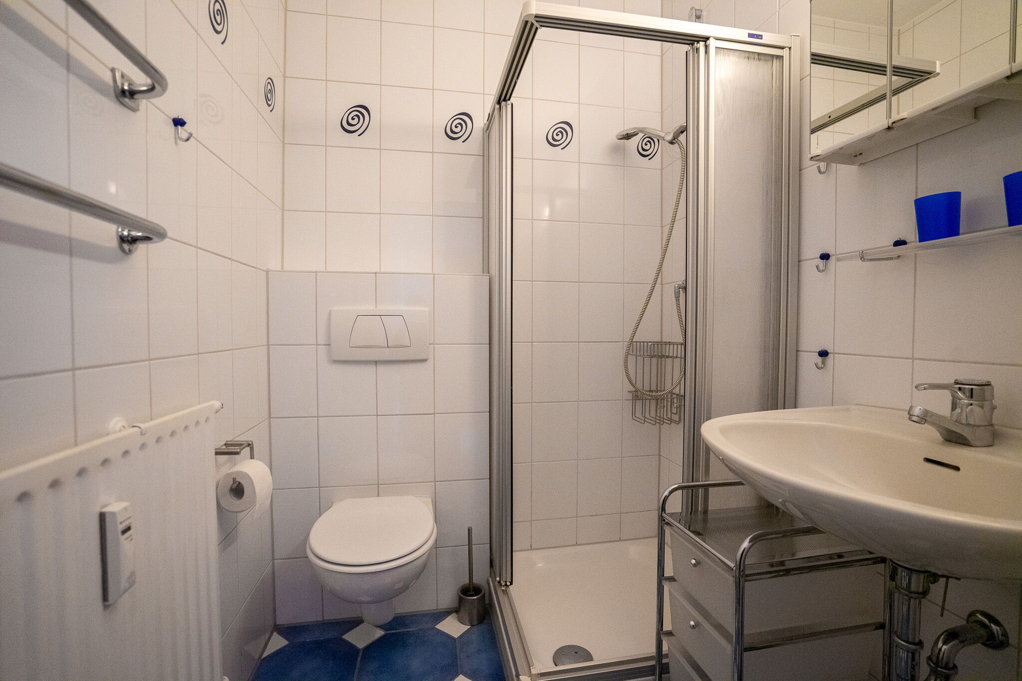 Ein Badezimmer mit Dusche, Toilette, Waschbecken und Handtuchheizkörper.