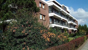 Ein mehrstöckiges Wohngebäude mit Balkonen, umgeben von üppigem Grün und blühenden Pflanzen.