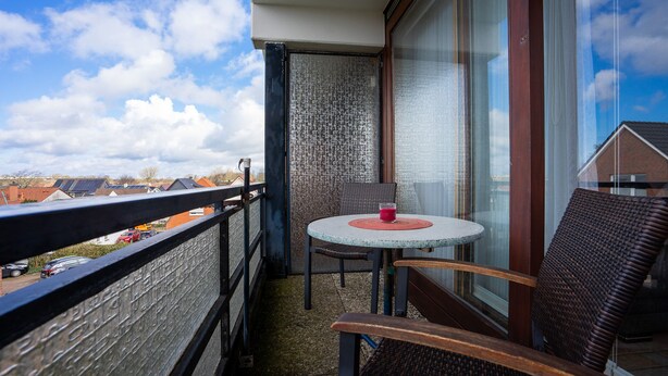 Ein Balkon mit rundem Tisch, zwei Stühlen und einem Glas roter Flüssigkeit.