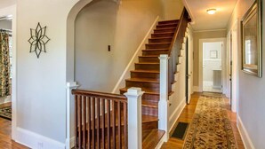 Un escalier avec des marches en bois et des rampes blanches, menant à un palier sur lequel se trouve un tapis à motifs.