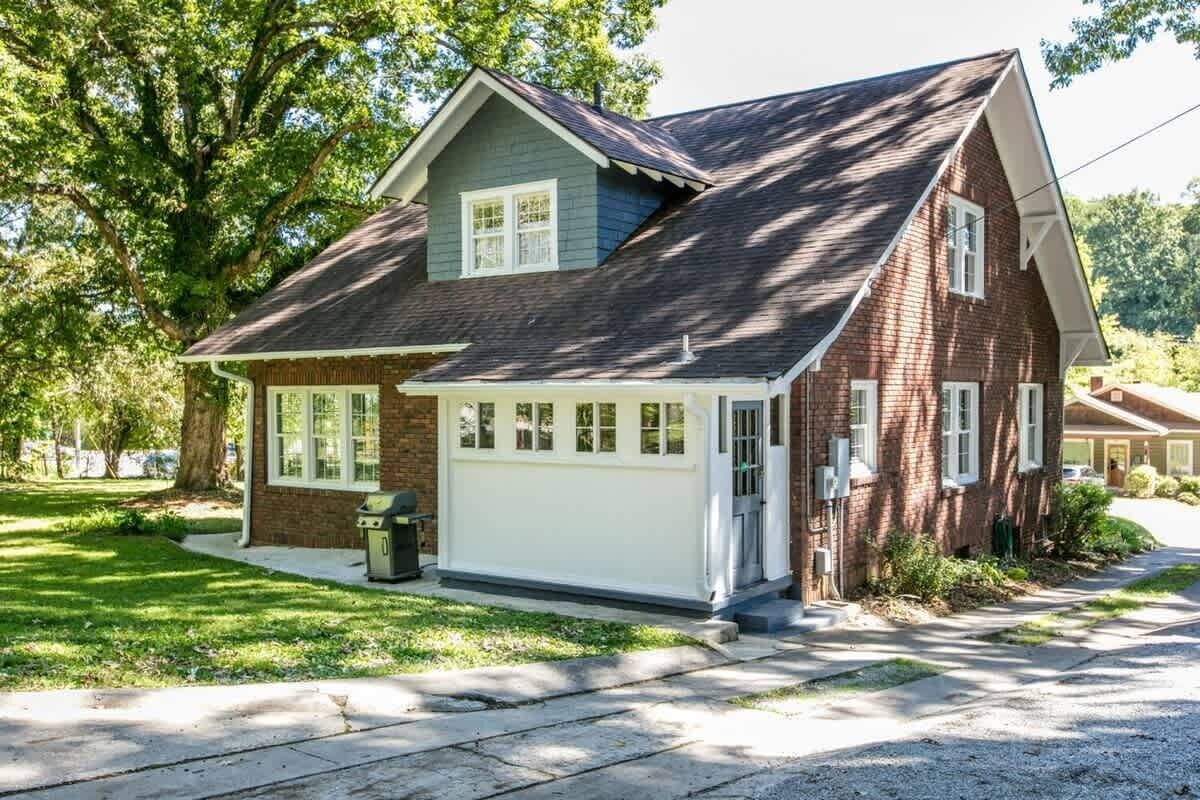 Ett tvåvåningshus med ett garage, en trädgård framför huset och ett stort träd.
