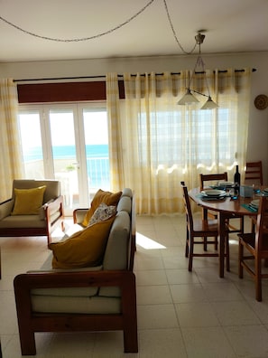 Relax in this inviting living area with a sofa, armchairs, and dining table, offering a view of the sea through large windows.