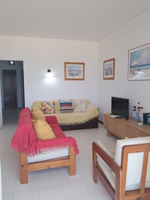 Ein Wohnzimmer mit einer Couch, einem Fernseher und einem Couchtisch. An der Wand hängen Bilder in Rahmen.