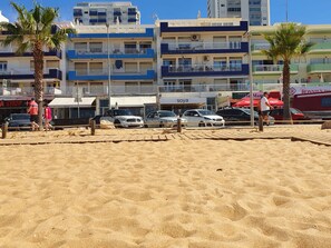 Ein Parkplatz direkt am Strand mit mehreren Autos, Palmen und einer Reihe mehrstöckiger Gebäude mit Balkonen.