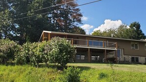 A two-story house with a balcony, surrounded by lush greenery and trees. - Hillside Haven (Penn Yan)
