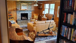 A cozy living room with a fireplace, leather sofas, a wooden coffee table, and a bookshelf filled with books. - Hillside Haven (Penn Yan)
