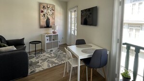 A modern living room with a sofa, a dining table with chairs, a small white cabinet, and artwork on the walls. - Charming one-bedroom apartment in the heart of the city (Guimarães)