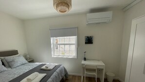 A bedroom with a bed, bedside table, lamp, window, and air conditioning unit. - Charming one-bedroom apartment in the heart of the city (Guimarães)