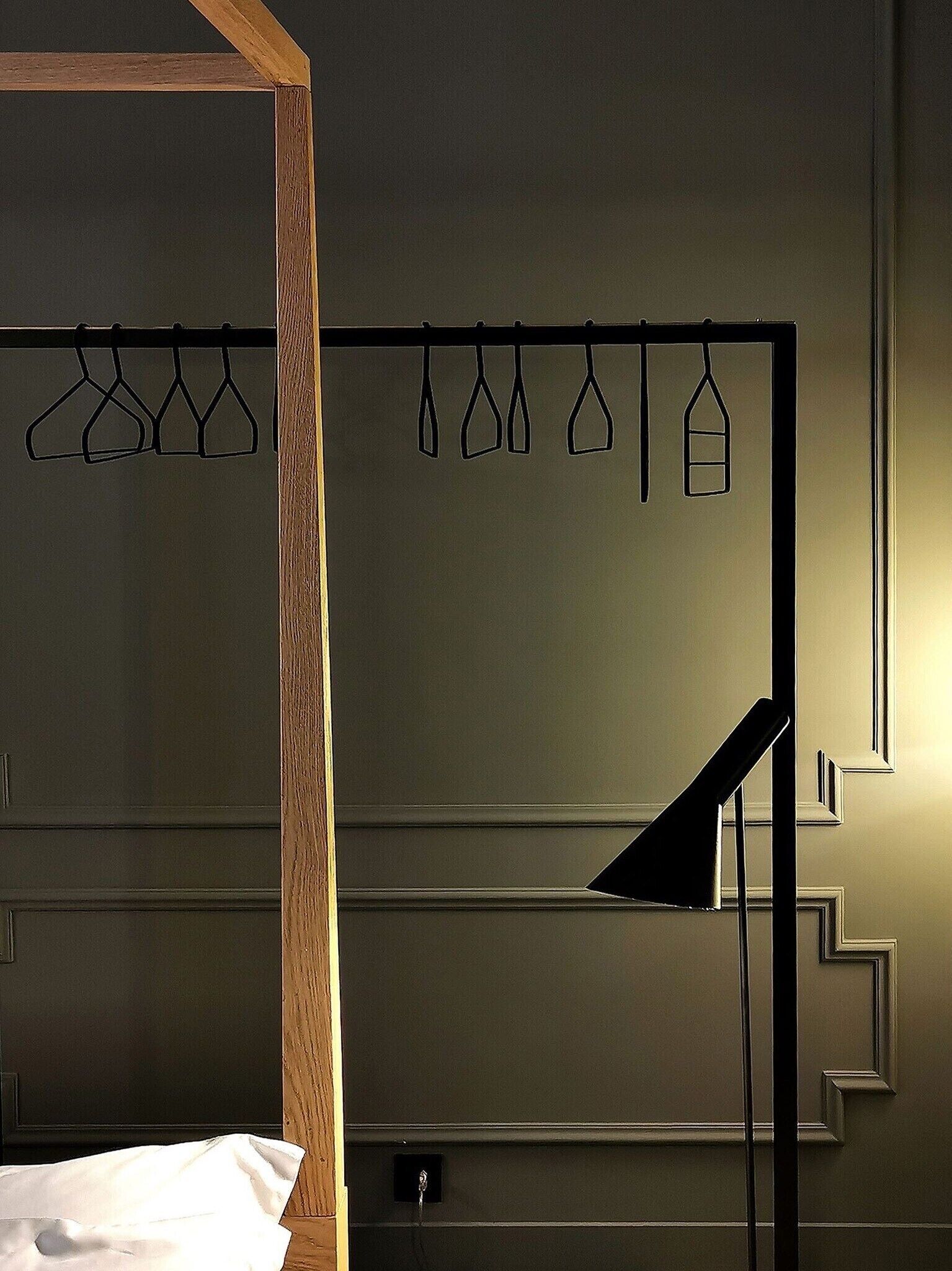 A bedroom with a wooden headboard, a bed, a hanging light fixture, and a wall-mounted coat rack with clothes.