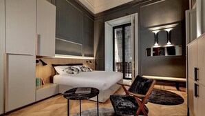 A modern bedroom with a bed, a chair, a small table, and built-in wardrobes. - Luxury apartment in the historic center (Catania)