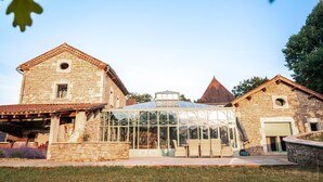 A stone building with a glass greenhouse, a covered patio, and a small garden area.