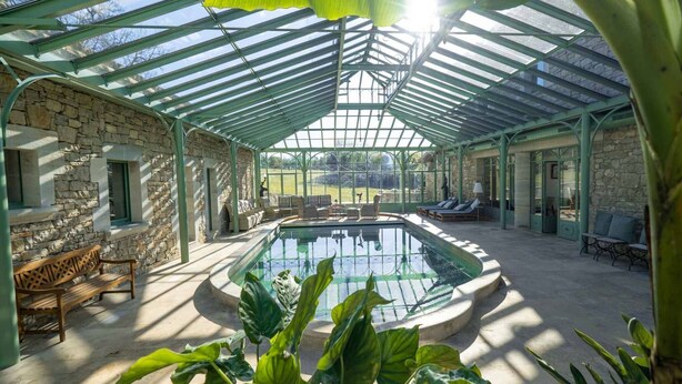 A covered outdoor pool area with stone walls, lounge chairs, and a glass ceiling.