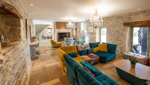 A spacious living room with a stone wall, a fireplace, and a staircase leading to an upper level.