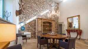A dining area with a stone wall, a chandelier, and a round wooden table with chairs.