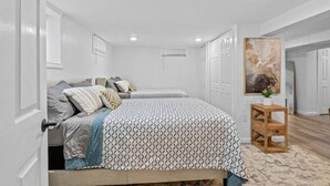 A bedroom with two beds, white walls, and a wooden floor.