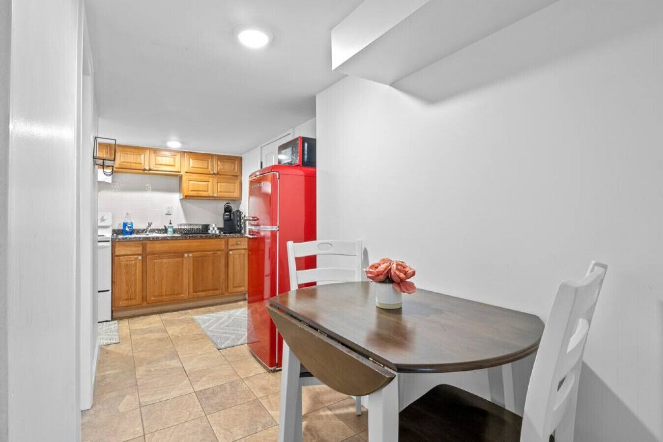 Une cuisine de taille réduite, dotée de meubles en bois, d’un réfrigérateur rouge et d’une table à manger avec des chaises.