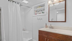 A modern bathroom with a walk-in shower, a vanity with a mirror, and a shelf with toiletries.