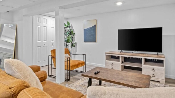 A modern living room with a large flat-screen TV, a wooden coffee table, and two armchairs.