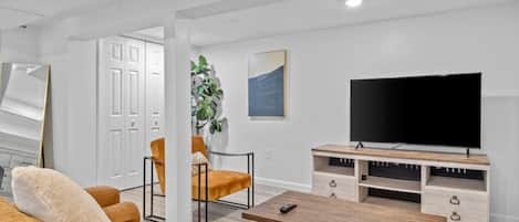 A modern living room with a large flat-screen TV, a wooden coffee table, and two armchairs.