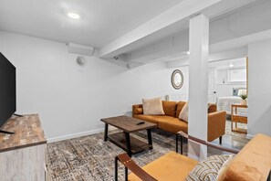 A modern living room with a sofa, coffee table, and a TV stand. - Sweet & Cozy Studio Apartment (South Burlington)