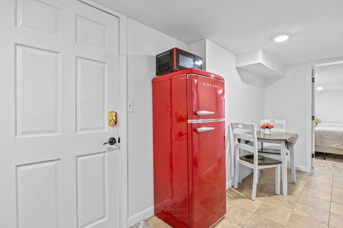 A compact room with a red refrigerator, white door, and a small dining area with a table and chairs.