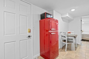 Une pièce de taille modeste, avec un réfrigérateur rouge, une porte blanche et un petit coin repas comprenant une table et des chaises.