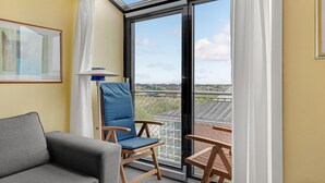 Ein Balkon mit Blick auf die Landschaft, ein graues Sofa, ein blauer Stuhl und ein kleiner Holztisch.