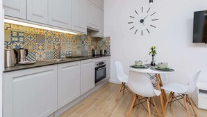 Uma cozinha moderna com armários brancos, um mosaico colorido, um relógio e uma área de jantar com cadeiras brancas e uma mesa pequena.
