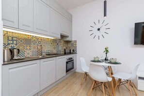 Una cocina moderna con armarios blancos, un salpicadero colorido, un reloj y un comedor con sillas blancas y una mesa pequeña.