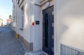 Un edificio con una puerta negra, un detector de incendios y una ventana pequeña.