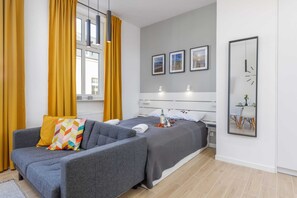 Een moderne slaapkamer met een grijze bank, een bed met een grijze dekbedovertrek, een nachtkastje met een lamp en een spiegel aan de muur.
