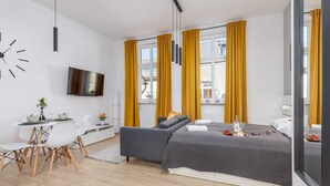 Quarto moderno com cama, televisão, escrivaninha e área de refeições.